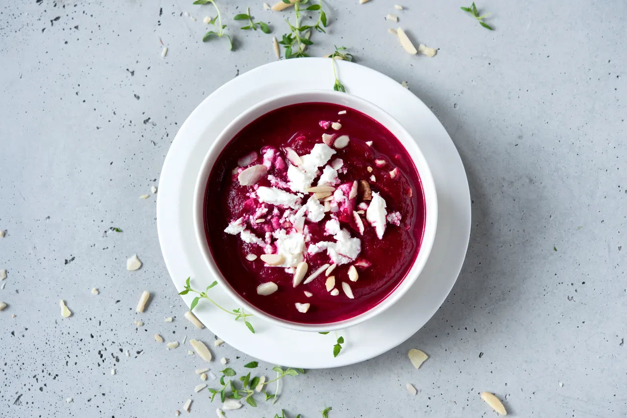 a whote bowl containing purple beetroot soup on a grey background